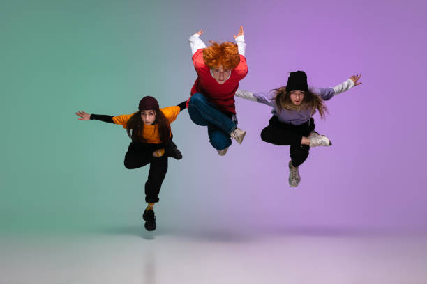 Group of teens, boys and girls dancing hip-hop in stylish clothes on gradient studio background in neon light. Group of teens, boys and girls dancing hip-hop in stylish clothes on colorful gradient studio background in neon light. Youth culture, movement, style and fashion, action. Fashionable portrait. rap kid stock pictures, royalty-free photos & images