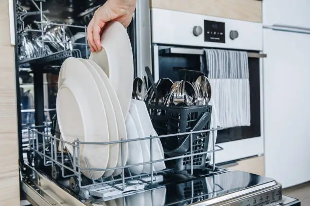 Woman loading the dishwasher. Open dishwasher with clean glasses and dishes close-up after washing. Clean  in open dishwashing machine.