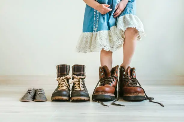 Photo of Close up of little girl in dress putting on father's hiking shoes