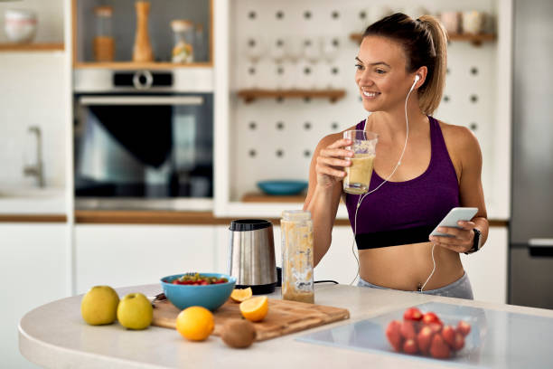 istock Happy sportswoman using smart phone while drinking smoothie in the kitchen. 1243466150
