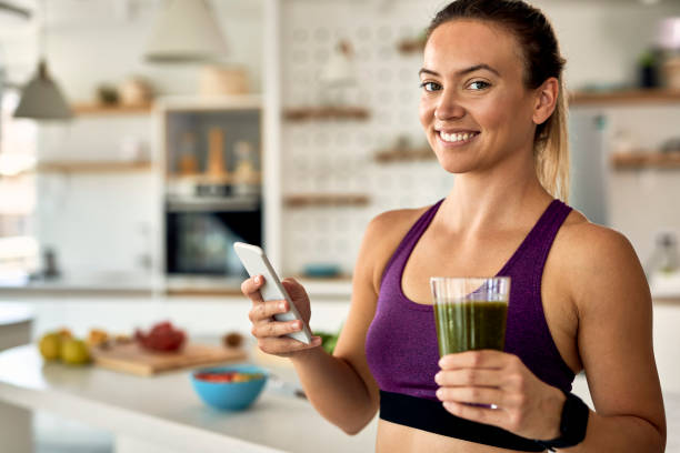 istock Happy athletic woman texting on cell phone while drinking smoothie in the kitchen. 1243467830