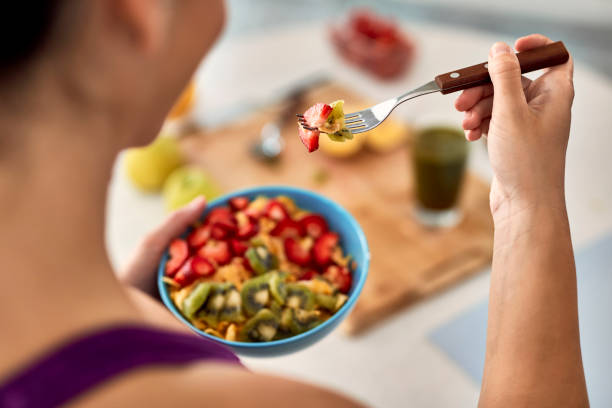 plan rapproché de femme mangeant la salade de fruit dans la cuisine. - routine foods and drinks clothing household equipment photos et images de collection