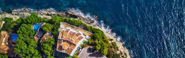istock Panoramic view directly from above coast and Mediterranean Sea. Summer luxury villas with swimming pools, parking area, sport tennis field. Mallorca or Majorca Island, Balearic Islands, España, Spain 1243472241