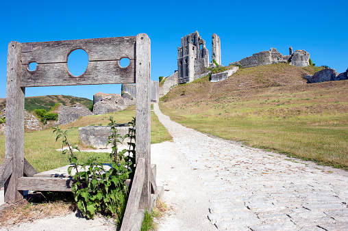 Corfe Castle, Isle of Purbeck, Dorset, England. Wooden stocks in front of the 11th Century Corfe Castle originally built by William the Conqueror. It was never defeated but eventually seized by Parliamentarians in the Civil War after betrayal from within, subsequently partially destroyed in 1646 by their order. Scenes on a woodland walk near Corfe Castle on the Purbeck Ridgeway in the Isle of Purbeck countryside an area of natural beauty, landscapes and scenery in Dorset, England, UK