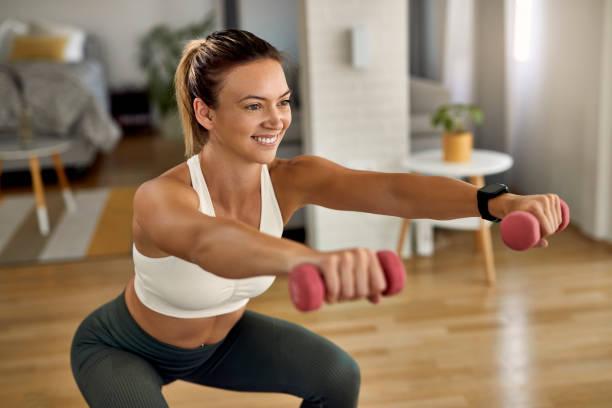 istock Happy athletic woman exercising with dumbbells while doing squats at home. 1243478882