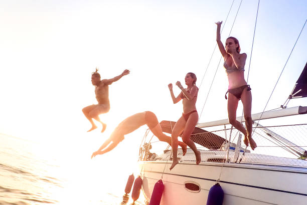 Young millenial friends jumping from sailboat at sea ocean trip - Guys and girls having summer fun together at sail boat party day - Luxury excursion concept on bright vivid filter with soft focus jóvenes amigos milenarios saltando desde el velero en el paseo marítimo por el océano - chicos y chicas divirtiéndose el verano juntos en el día de la fiesta del barco de vela - concepto de excursión de lujo en filtro vívido brillante con enfoque su
