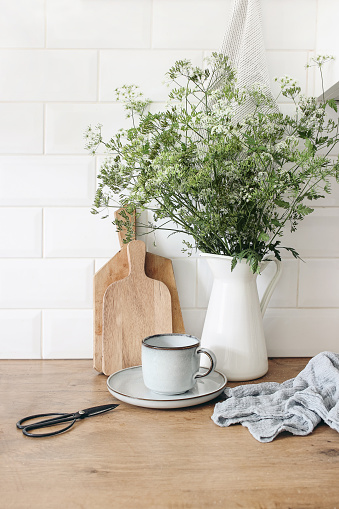 Rustic kitchen interior. Still life composition with cup of coffee, wooden chopping boards and cow parsley bouquet in jug. White brick wall, metro tiles. Scandinavian design, home staging, concept