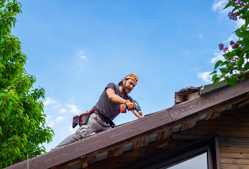 Man working on roof using electric screwdriver.