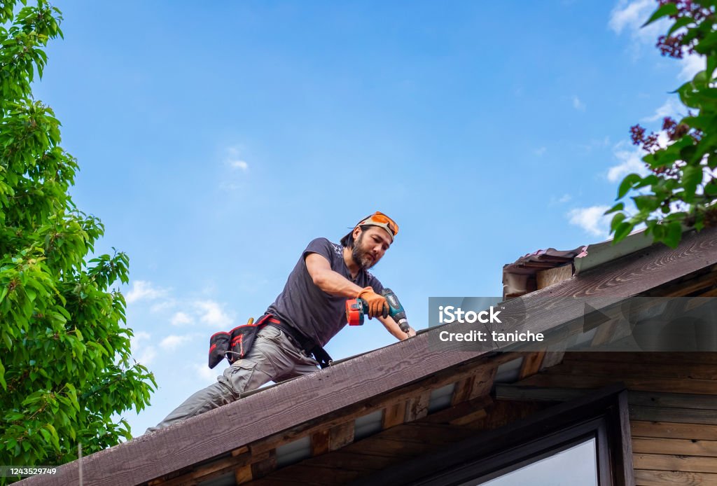 Man working on roof using electric screwdriver Man working on roof using electric screwdriver. Repairing Stock Photo