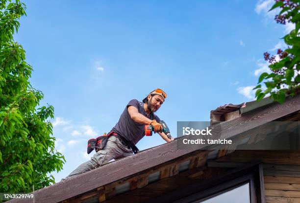 Man Working On Roof Using Electric Screwdriver Stock Photo - Download Image Now - Repairing, Rooftop, Residential Building