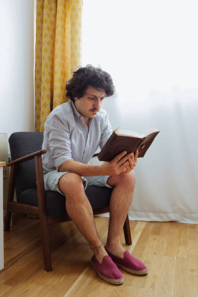 istock Handsome man reading a book sitting in a reading armchair 1243610978