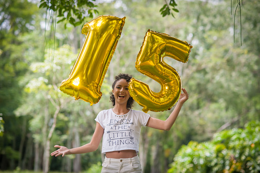 Brazilian teenager girl in the park trowing up  balloons number 15  in celebration of her fifteenth birthday