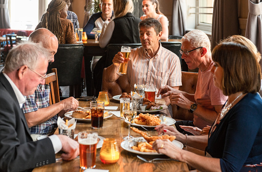 A group of friends in their 50s and 60s enjoying a meal and a drink in an English pub.