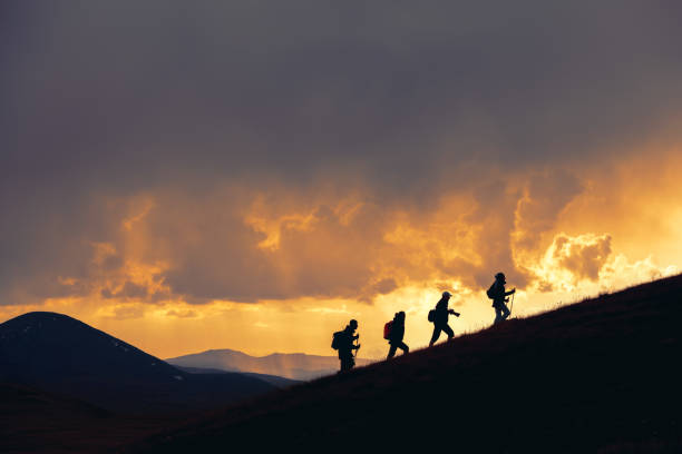 gruppe von wanderern wandert bei majestätischem sonnenuntergang in den bergen - people traveling journey group of people hiking stock-fotos und bilder