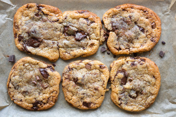 Freshly baked gooey chocolate chip cookies on a baking sheet A flat baking sheet lined with greaseproof paper holds six freshly baked chocolate chip cookies. The chocolate in the cookies has melted leaving the biscuits gooey. There are chocolate smears and stray chocolate chips on the tray around the cookies. chocolate chip cookie top view stock pictures, royalty-free photos & images