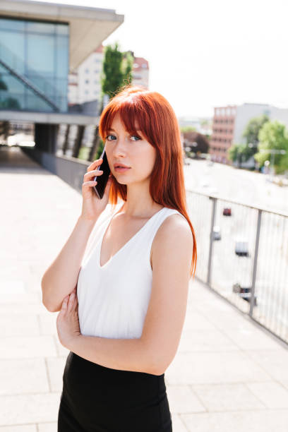 istock Red-haired girl talks on phone and looks at camera 1243646628