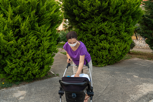 mother with masked newborn baby walks outside in her stroller