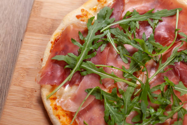 istock Pizza with prosciutto, cheese and arugula on wooden board 1243664034