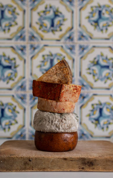 Different kinds of cheese. Assorted cheese tower on a wooden board in in front of a rustic tile wall.