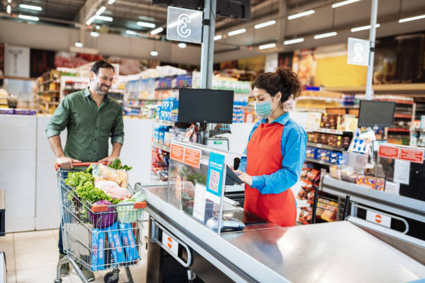 käufer mit schützender gesichtsmaske im supermarkt während coronavirus covid-19 pandemie - kassiererin supermarkt stock-fotos und bilder
