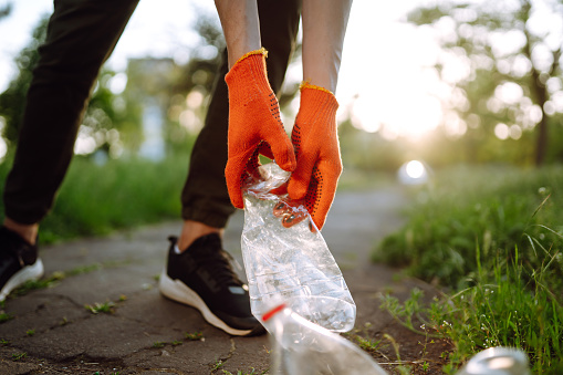 Men hand collects plastic trash for cleaning in the park. Volunteer wearing protective gloves collects bottle plastic. Environmental protection, ecological concept. Waste recycling.