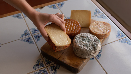 Hand selecting a cheese from a table with a variety of cheeses, on a traditional tile countertop.