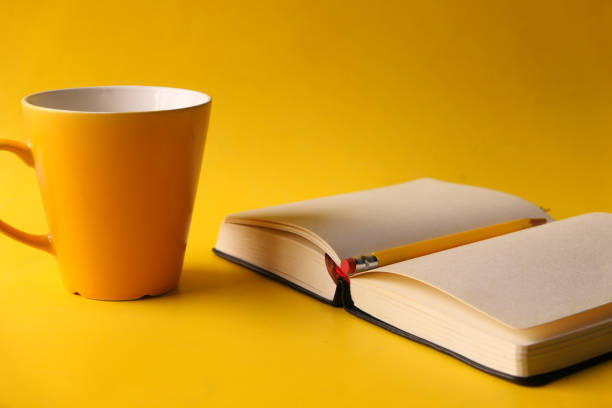 notepad with pencil and coffee mug on yellow background .