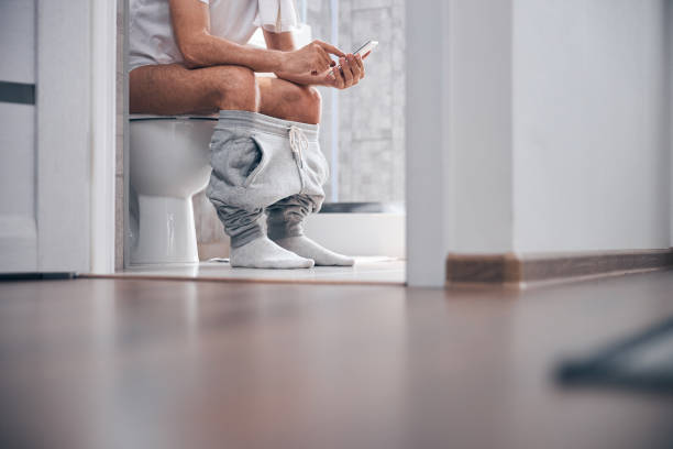 Man using his gadget in the water closet Cropped photo of a Caucasian male with a cellular phone sitting on the toilet seat toilet stock pictures, royalty-free photos & images
