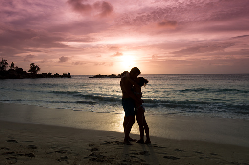 Young couple are kissing in a beautiful sunset in the tropical beach Petite Anse Kerlan in Praslin Island, Seychelles.