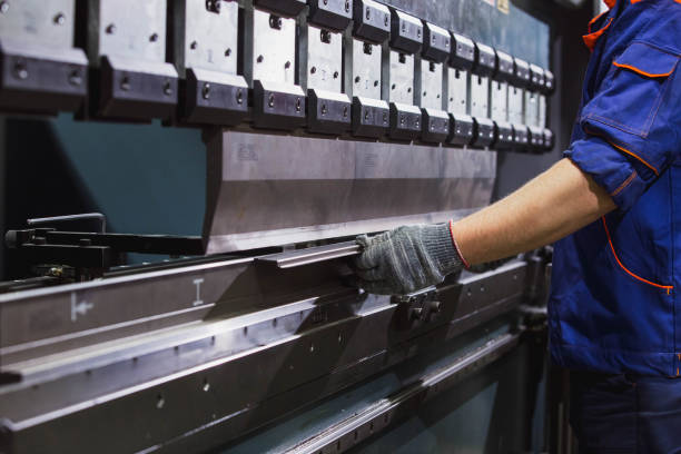 homme travaillant avec la tôle sur le frein hydraulique de presse de cnc. il met la pièce et la plie dans une grande machine à un angle - bending metal cnc steel photos et images de collection