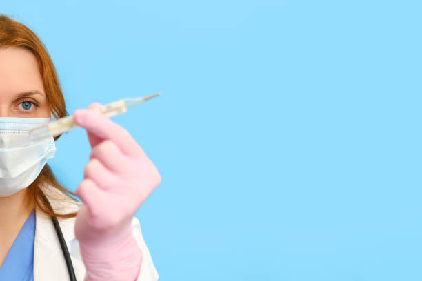 istock Doctor in a white uniform with a thermometer in his hand on a blue background, copy space. 1243786825