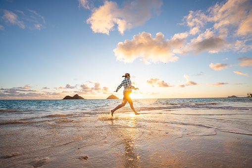 Woman runs along the beach at sunrise