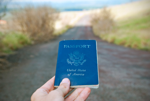 American passport held up above an open road