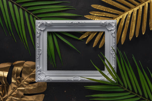 istock Creative layout with gold and green tropical palm leaves with white frame on black background. Minimal summer abstract pattern. 1243808054