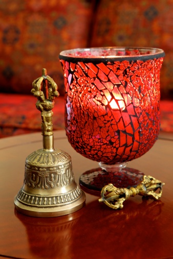 Dubai, UAE - Close-up of an ornate glass candle holder with a lit candle inside emanating a warm light. By its side is a Buddhist Tibetan prayer bell. The items have been placed on a Chinese rosewood coffee table.