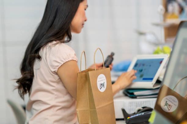 Young female shop owner using POS system on a digital tablet to enter products for a customer to purchase Asian retail manager entering products into a point of sale terminal point of sale tablet stock pictures, royalty-free photos & images