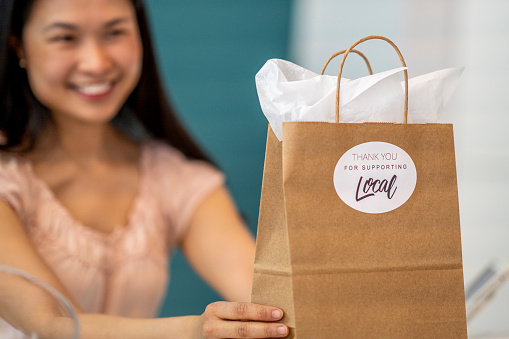 Sonriente mujer propietaria de la tienda sosteniendo una bolsa de artesanía con una etiqueta adhesiva 