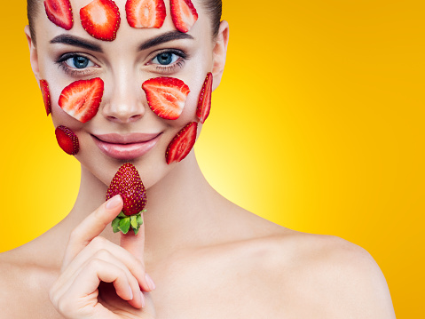 Happy young girl with facial mask of strawberry on her face