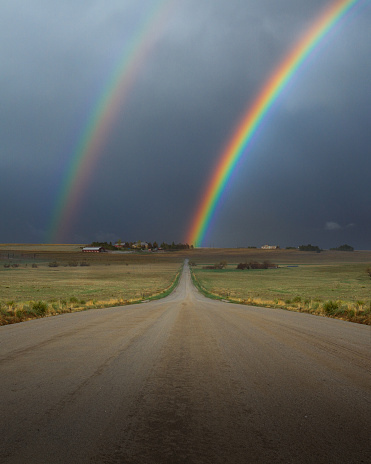 A rainbow intersects a country road in Colorado perfectly in a serendipitous moment.