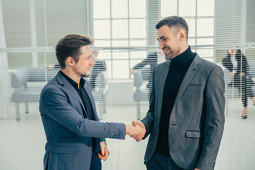 Welcome to our team. young modern men in smart casual wear shaking hands. Two smiling businessmen shaking hands together. Two confident businessmen shaking hands at the outside of the office.