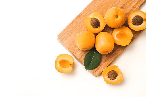Fresh ripe apricots halves and whole fruits on cutting board on white background with copy space