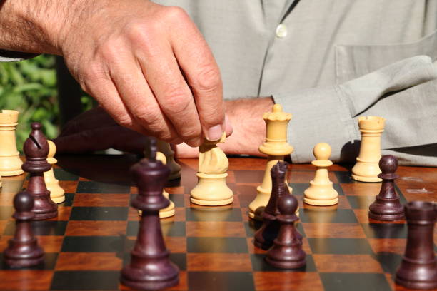 A chess board, a man with a grey shirt moving a piece