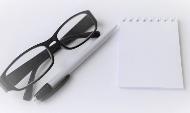 istock Blurred template for text on a notepad on a white background, with a white pen and black-rimmed glasses lying next to it 1243921857