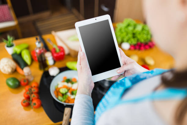istock Woman using empty screen digital tablet while preparing healthy meal in kitchen. Online recipe concept. 1243933860