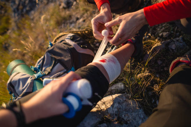 Woman getting first aid treatment after a hiking injury Female hiker sitting on a rock while her partner puts on first aid on her injury man sitting with a bandage on his leg stock pictures, royalty-free photos & images