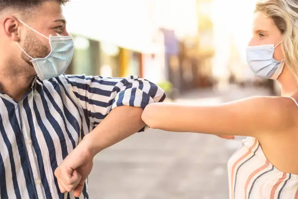 Photo of Young friends wearing face surgical mask doing new social distancing greet with elbow for preventing corona virus outbreak - Physical distance and safety greetings concept