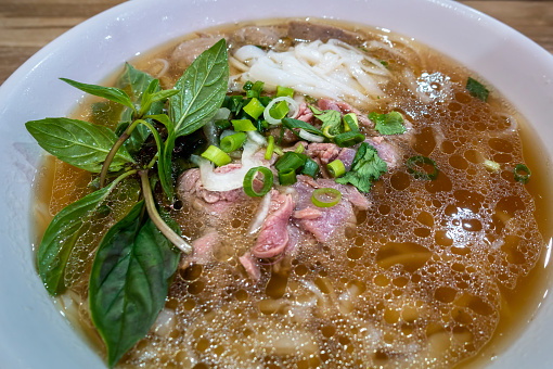 Vietnamese beef rice noodle soup (Pho Bo) – boiling hot fragrant stock with a variety of herbs is added to sliced raw beef. Contains spices, cilantro, scallion and mint. Lime wedges separated served.