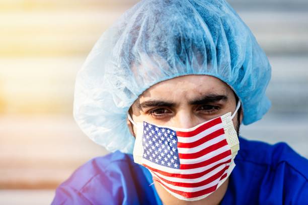 grave surmené, jeune travailleur de santé masculin un masque de protection drapeau américain regardant la caméra - depression sadness usa american flag photos et images de collection