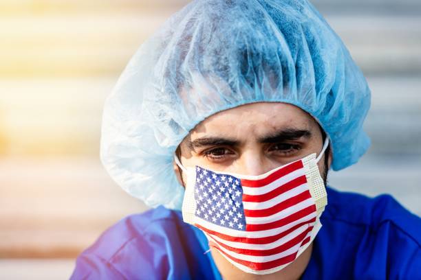 gravemente troppo lavoro, giovane operatore sanitario maschile una maschera protettiva bandiera degli stati uniti guardando la fotocamera - depression sadness usa american flag foto e immagini stock