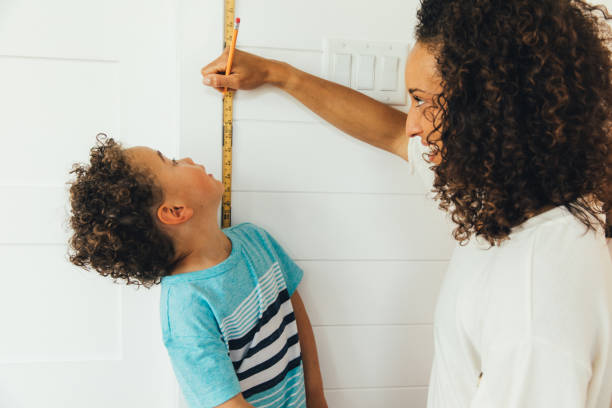 Mother Measuring Height of Son A mom measures her son against a ruler and wall to see how tall he is inside their home. The boy is growing fast at 4 years old and is excited to grow and learn with his mom teaching him. boy height measure stock pictures, royalty-free photos & images